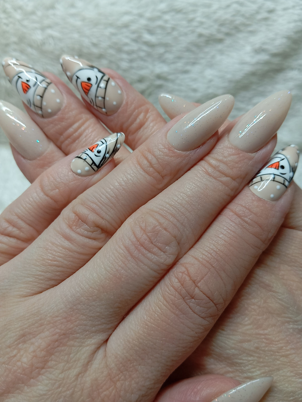 Manucure press-on nails beige scintillante avec bonshommes de neige portée sur les deux mains